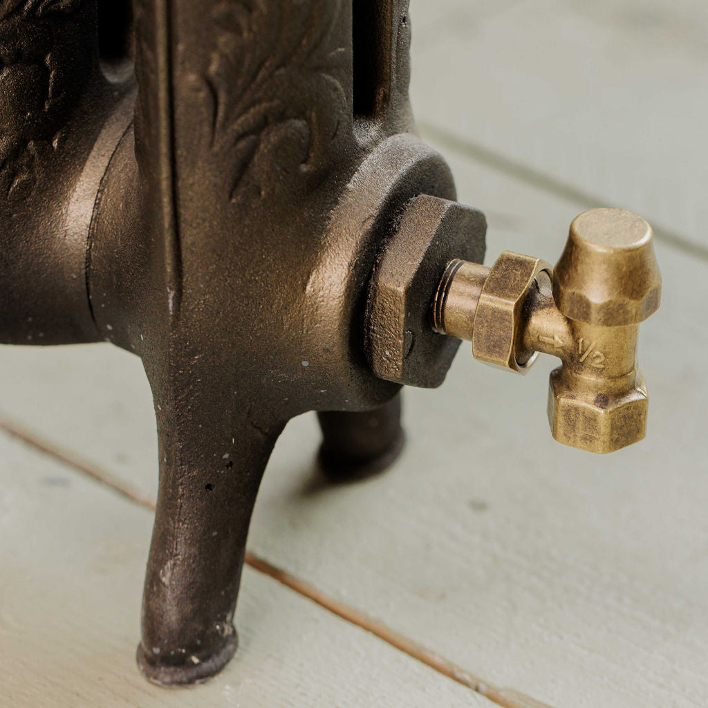 Close-up of a vintage cast iron radiator with an ornate brass lockshield valve on a light green painted wooden floor