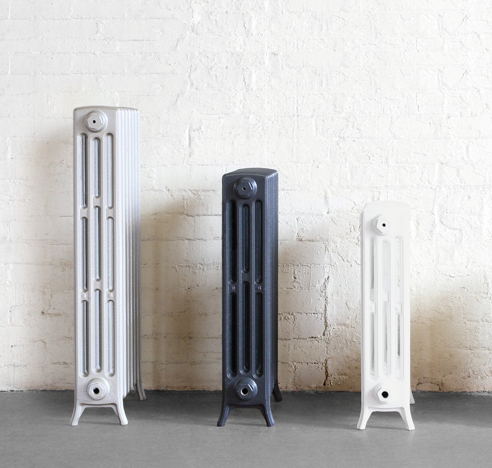 Four new cast iron radiators sat in sunlight next to a piano and antique furniture